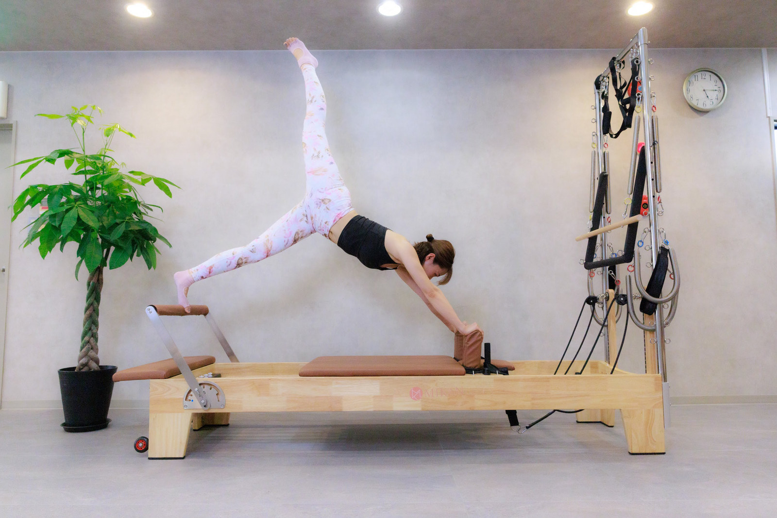 リフォーマーの上で片脚を高く上げたポーズをとる女性(ALOHA YOGA マシンピラティススタジオ)